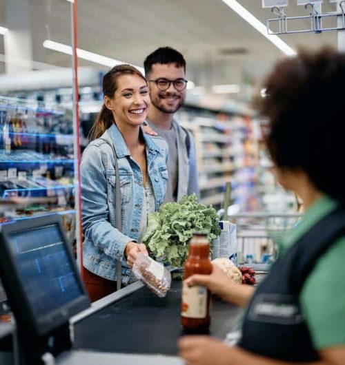 young-happy-couple-talking-to-cashier-at-supermarket-checkout-1-1.jpg